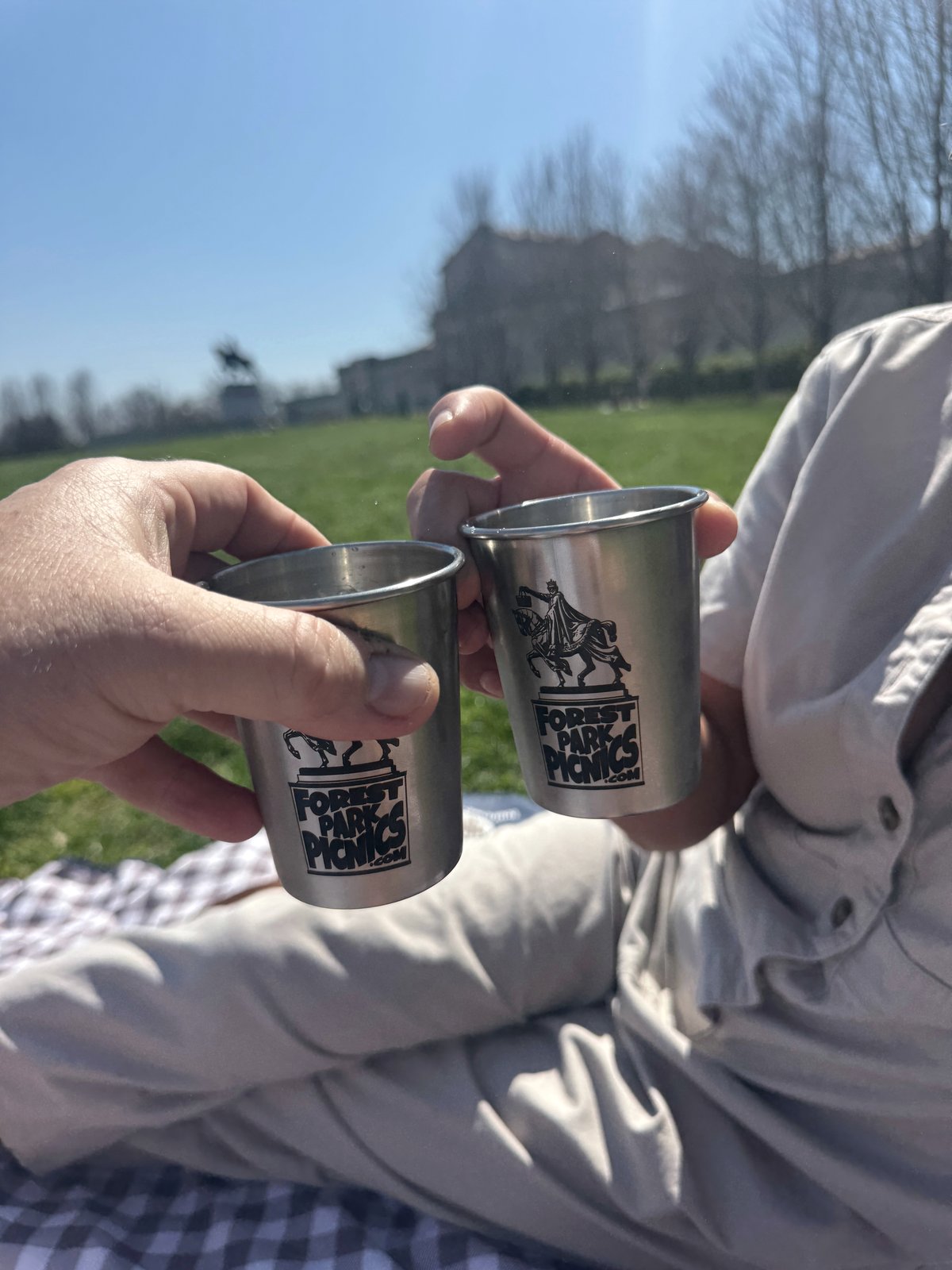 Two Forest Park Picnics branded cups being toasted with the Apotheosis of King Louis IX statue and the St. Louis Art Museum visible in the background on Art Hill