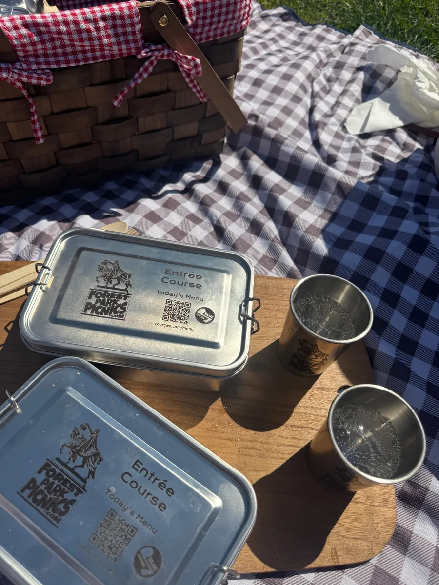 Forest Park Picnics entrée course tins and branded cups laid out on a wood board at Art Hill
